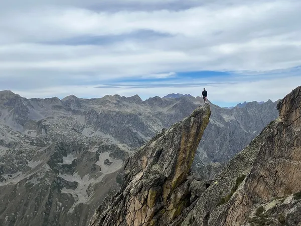 Andrea Murisasco in piedi sulla punta di una cresta rocciosa, con le montagne alle spalle